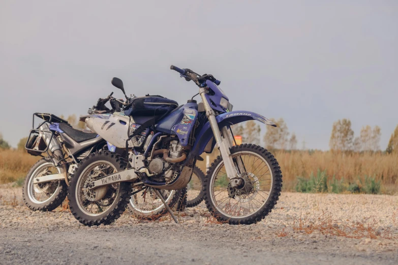 two motorbikes sit together in a dirt field