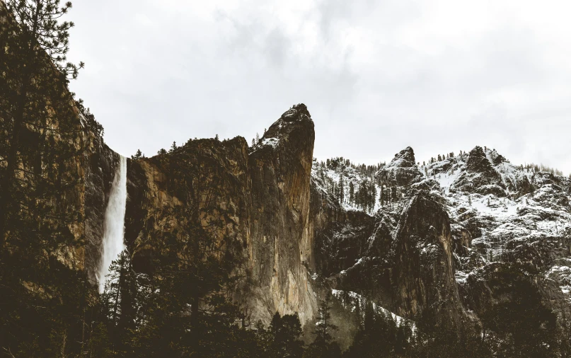 a tall waterfall is surrounded by snow covered mountains