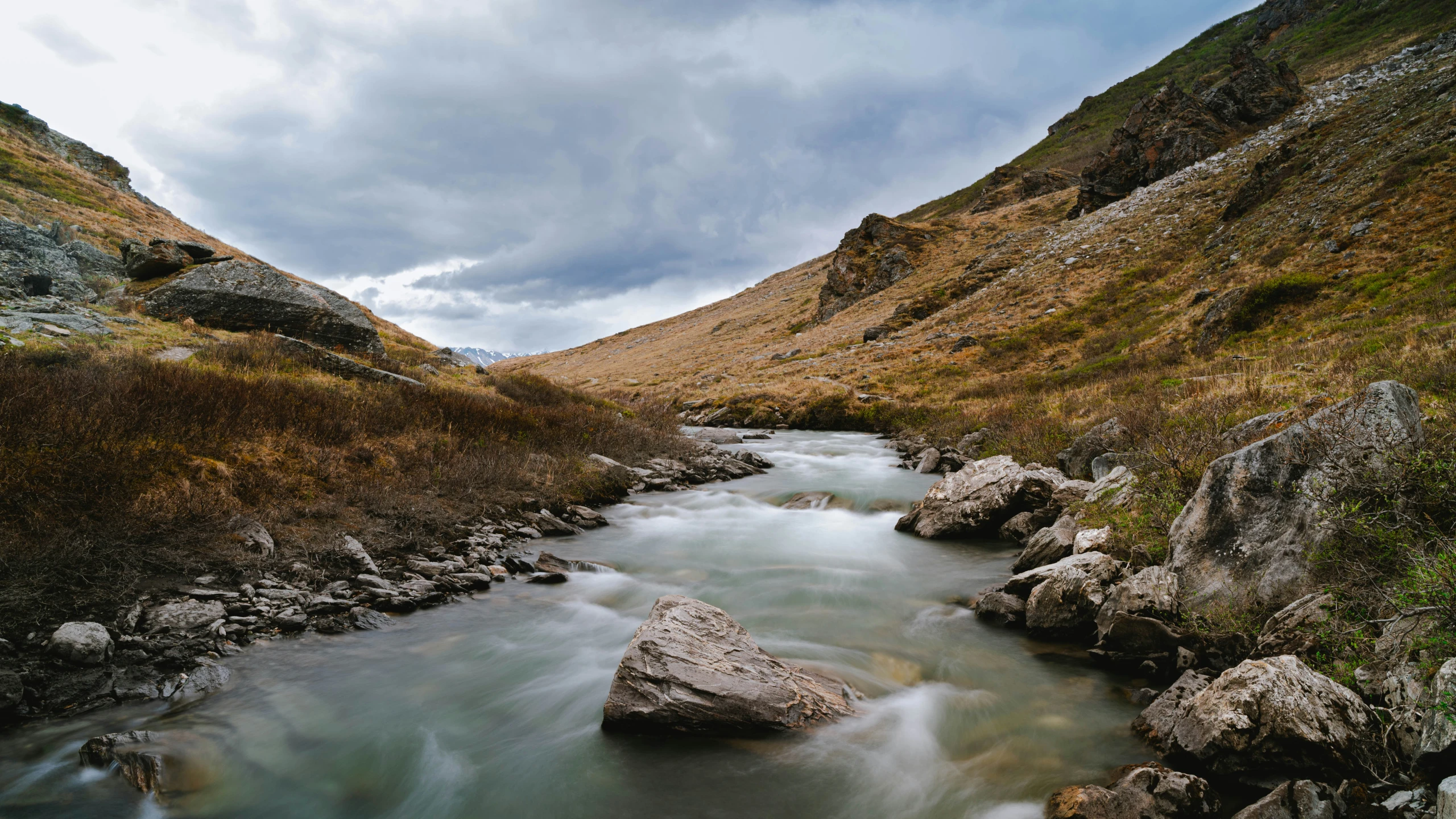 river near a rocky slope with grass and trees