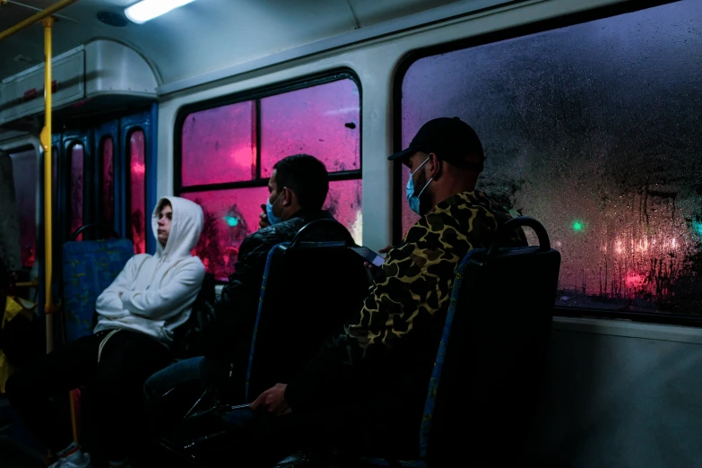 two men sit on a train, one in a white hooded hoodie and one in a green hoodie