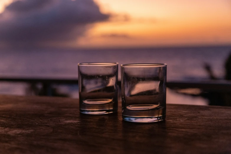 two s glasses sitting on a table facing a sunset