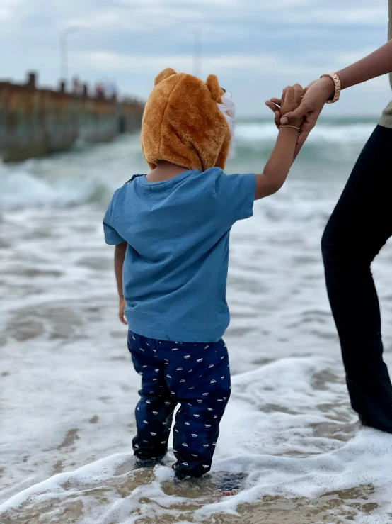 the little boy is holding the woman's hand while he walks along the beach