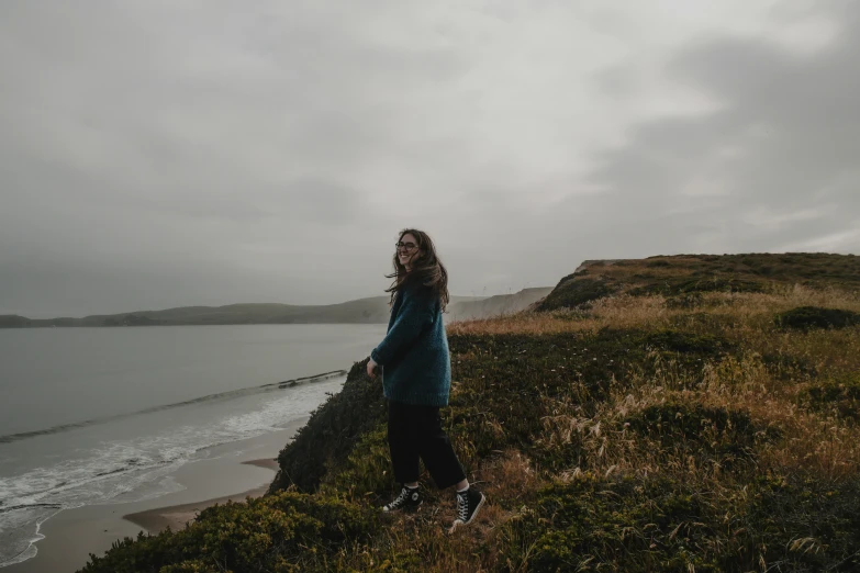 a woman standing on top of a grass covered hillside near water