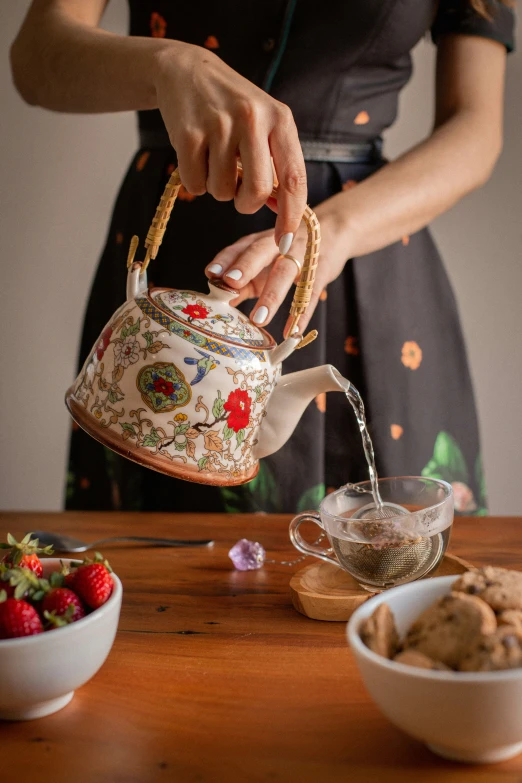 a woman pours a teapot over a bowl of cookies