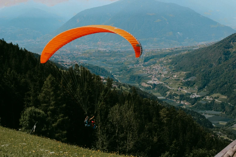 an orange paraglider glides over a green field