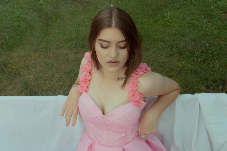 the woman wearing a pink dress with ruffles sits on a white sheet