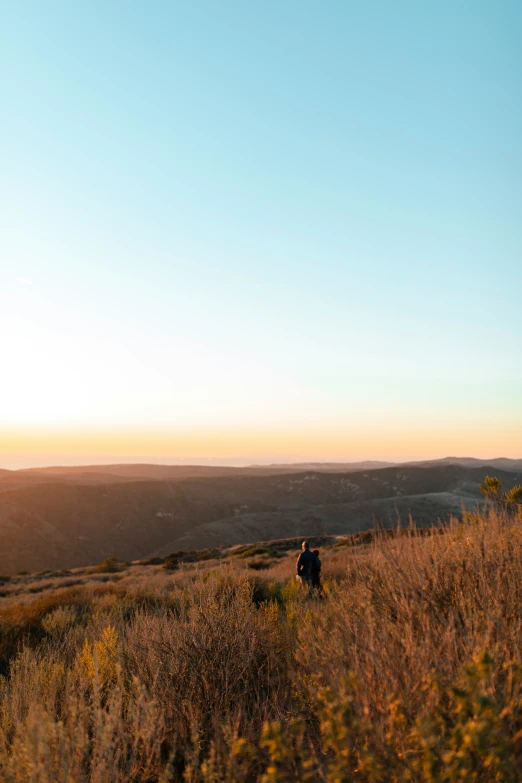 two people walking across a grass field on top of a hill