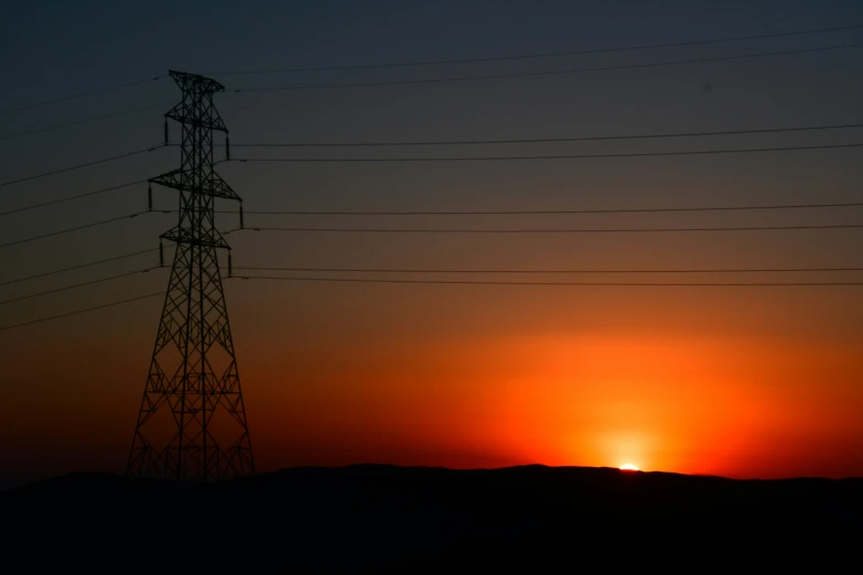 power lines are silhouetted against the sun setting over the plains