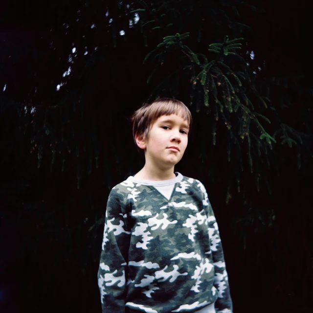 a  wearing a green camo top with frisbees next to trees