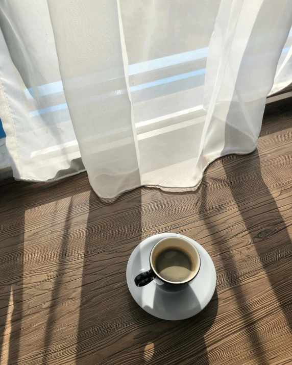 a white cup is on the brown carpet by a window