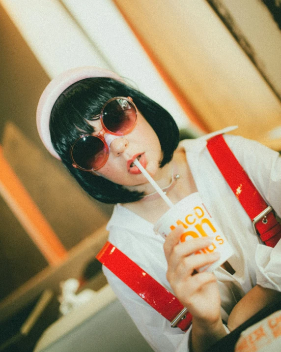 a woman with short black hair wearing sunglasses drinking a drink