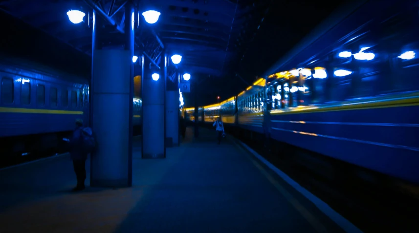 a blue train with headlights at night is passing through the station