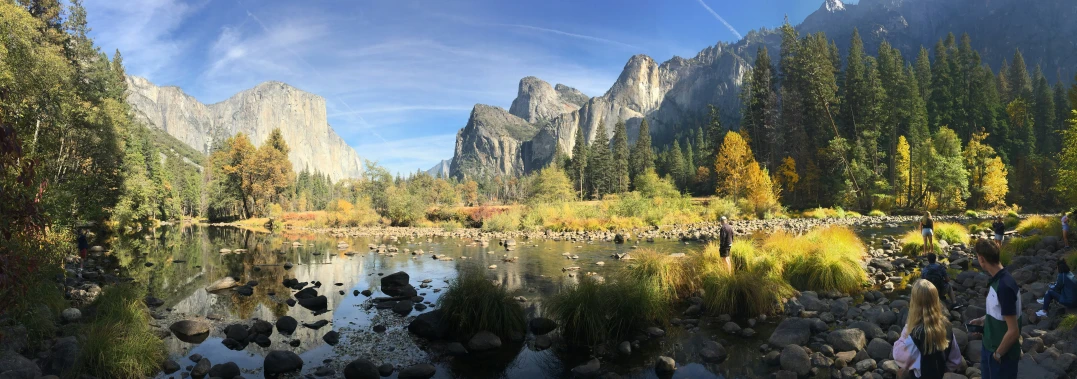 a group of people stand by a lake near mountains