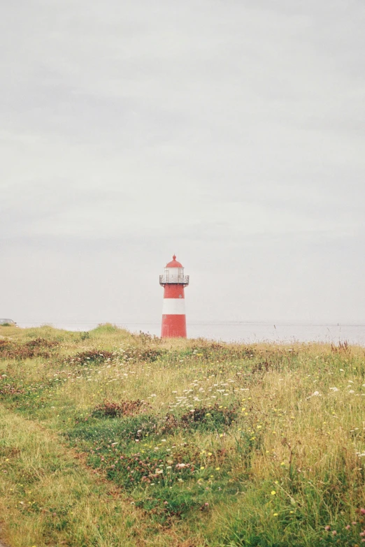 a large grassy hill with a red and white lighthouse in the background