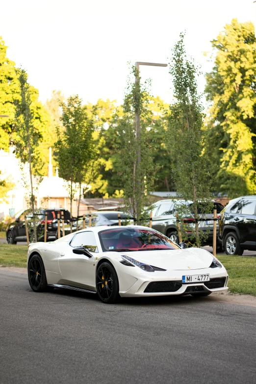 a white sports car driving down a street in front of a tree covered hillside