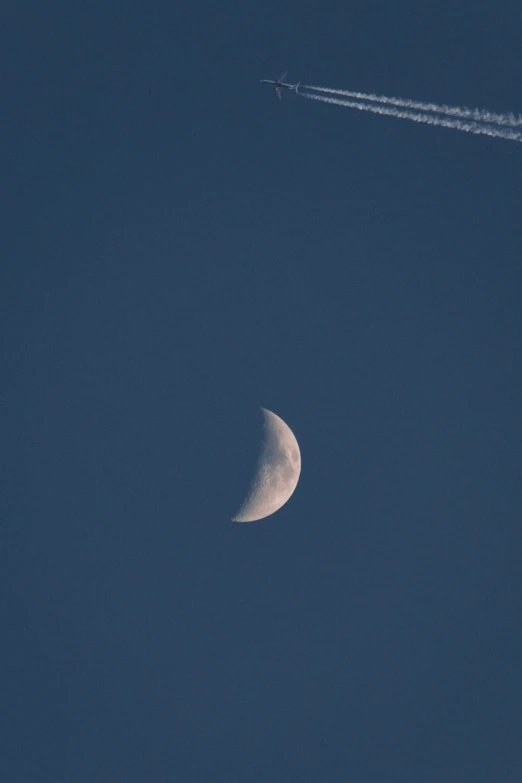 a contrails through the sky with the moon and plane