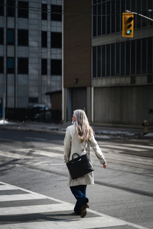 a woman in a white coat and blue jeans crossing a street