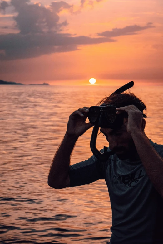 a man holding a camera up to his face as the sun sets