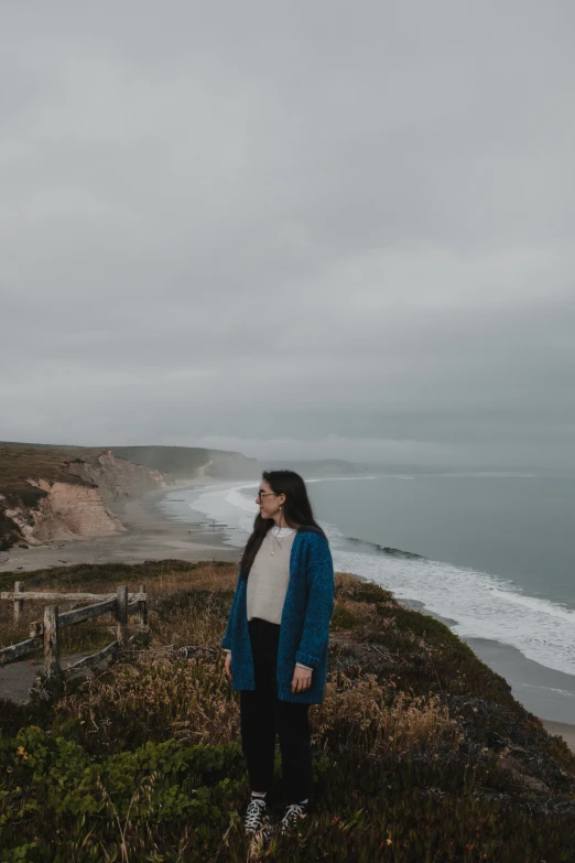 a girl is standing on a grassy hill near the ocean