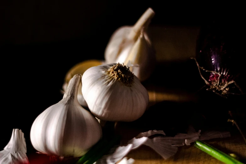 garlic sits on a  board next to onion stalks