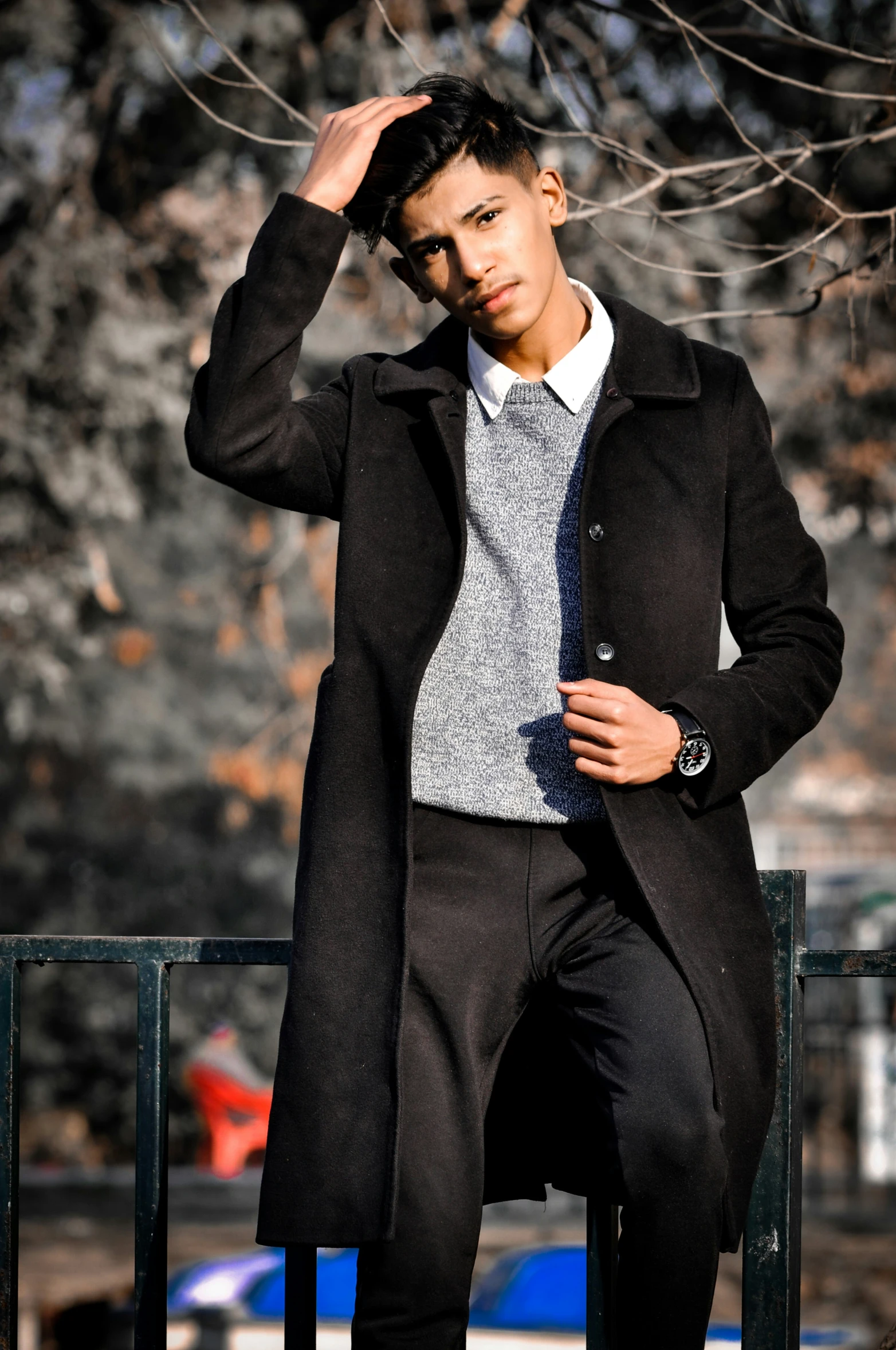 a young man leaning against a fence, with his hands on his head