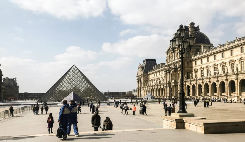 people walking in front of the egyptian museum, with a pyramid behind them