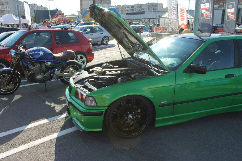 green car with engine compartment open and other cars in parking lot