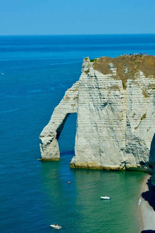 a cliff is on the sea, while boats are in the water