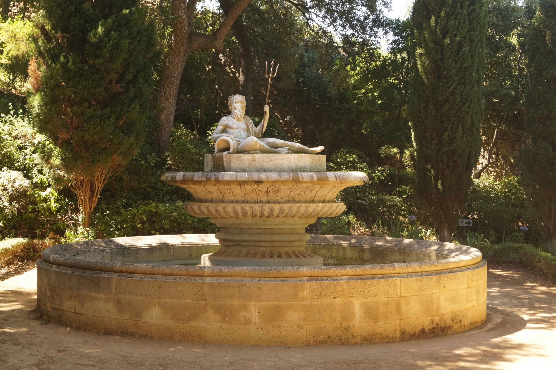a statue sits on a stone fountain surrounded by trees