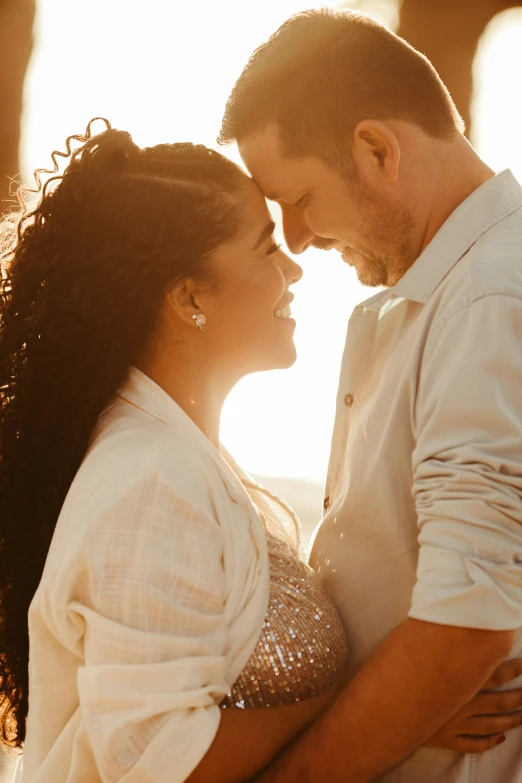 an attractive couple holding each other as the sun goes down behind them