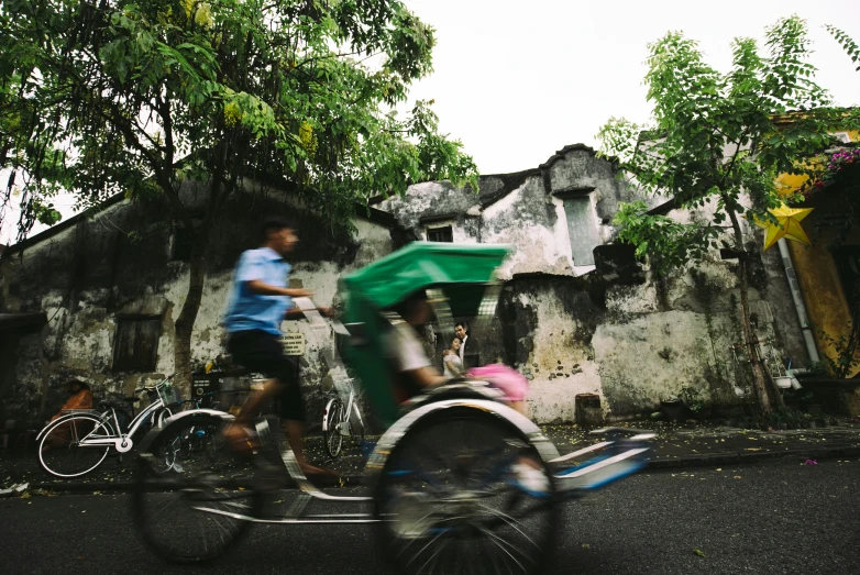 a boy and a girl ride on a tricycle through a street