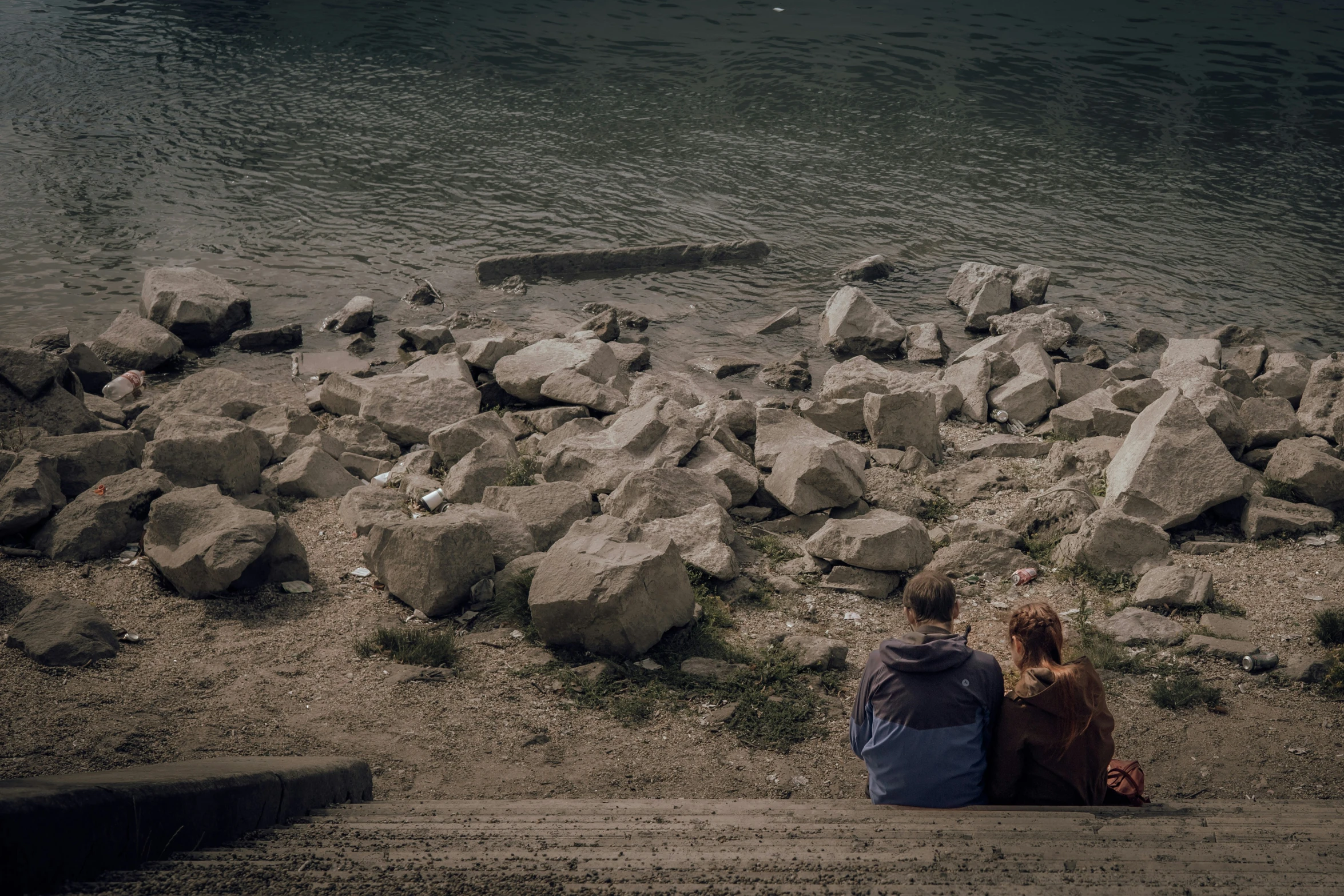 two people are sitting on the bank by the water