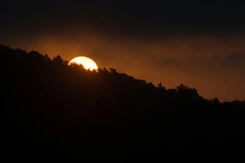 the sun is setting in front of the trees on a hill