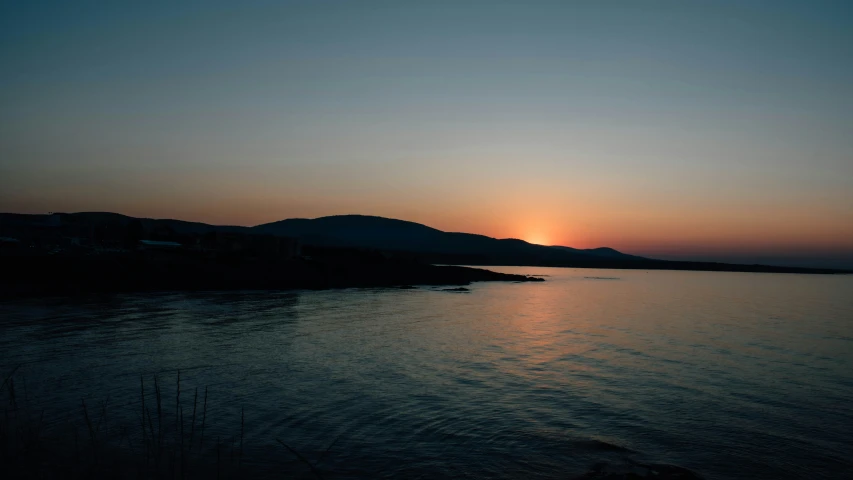 the sun setting on a lake near some hills