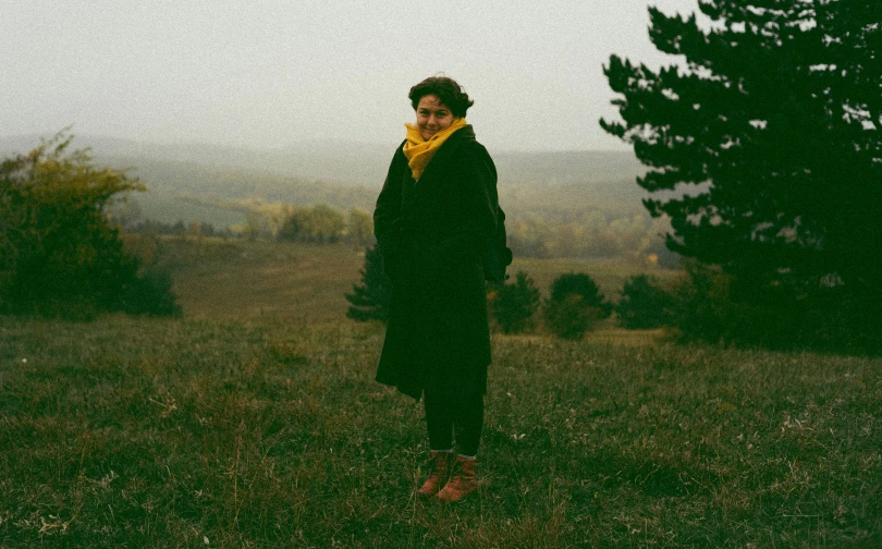 a woman in black dress and yellow scarf standing on a hill