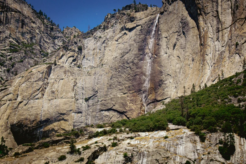 large waterfall pouring into the mountains near a forest