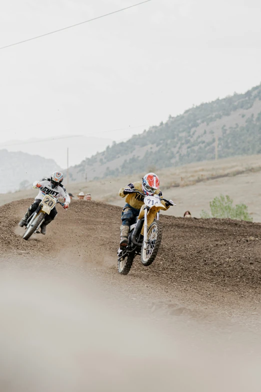 a couple of people riding motorcycles on a dirt track