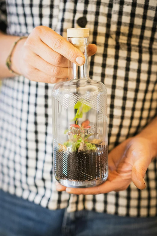 a man holds a small bottle filled with plants