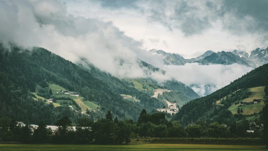 a mountain area with trees, houses, and clouds