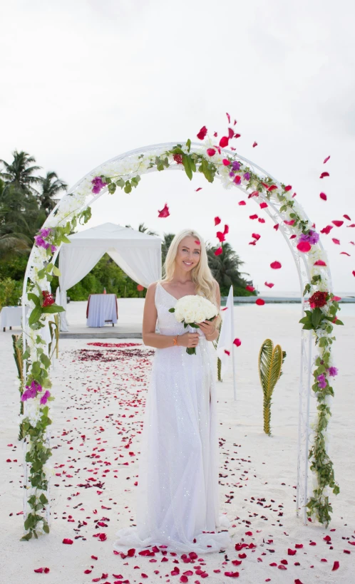 a woman in white and pink dress posing under an archway decorated with flowers