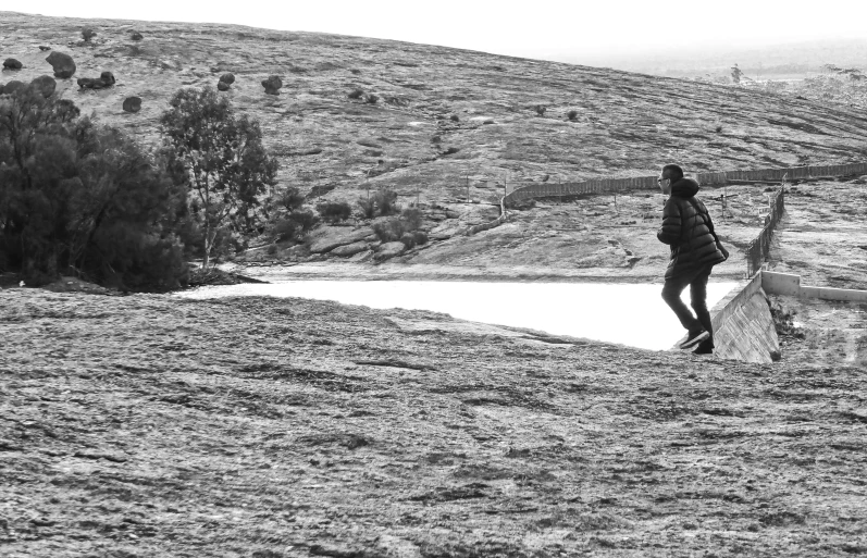 man with surfboard walking by a small lake