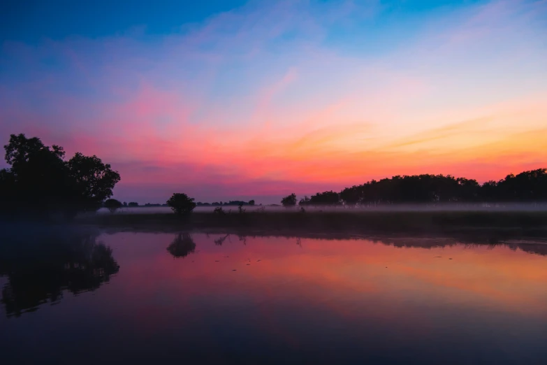 a sunset over a lake in the middle of a forest