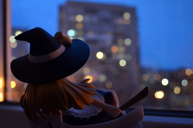 toy with hat sitting in window and city lights in background