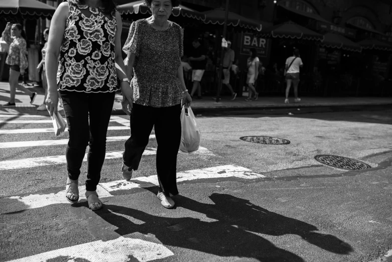 a woman walks across the road while another holds up a bag