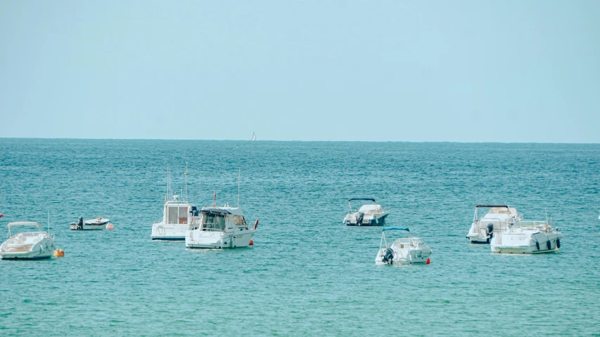 several small boats in the ocean with a sky background
