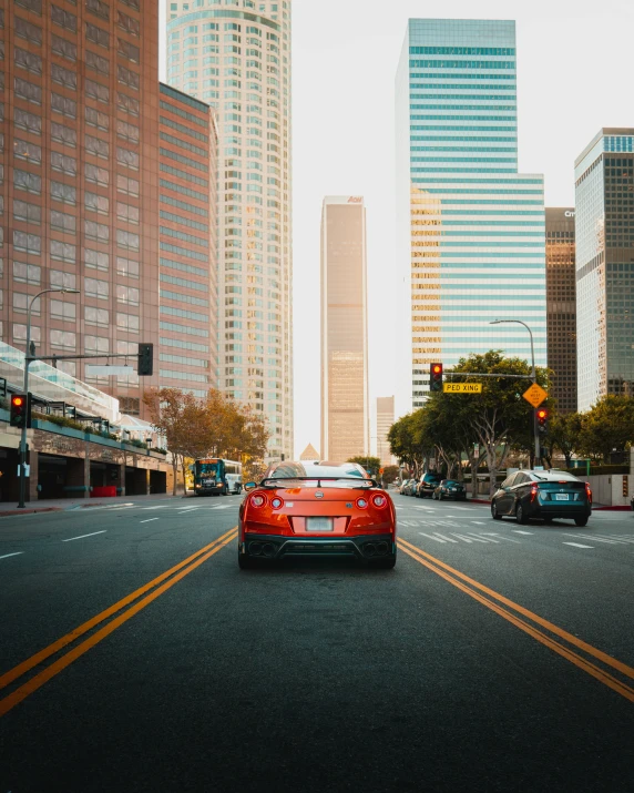 red car driving down the road in front of tall buildings