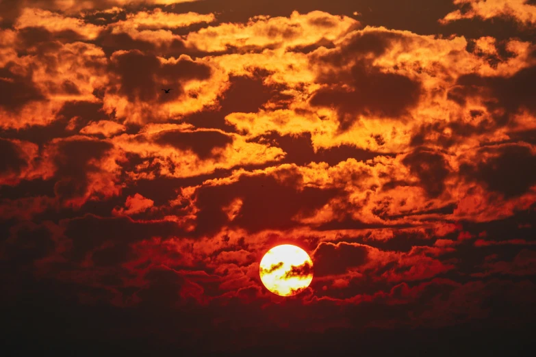 a sun setting behind clouds and a jet in the distance