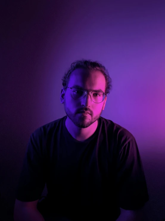 a man with glasses and a beard, sitting in front of a bright purple light