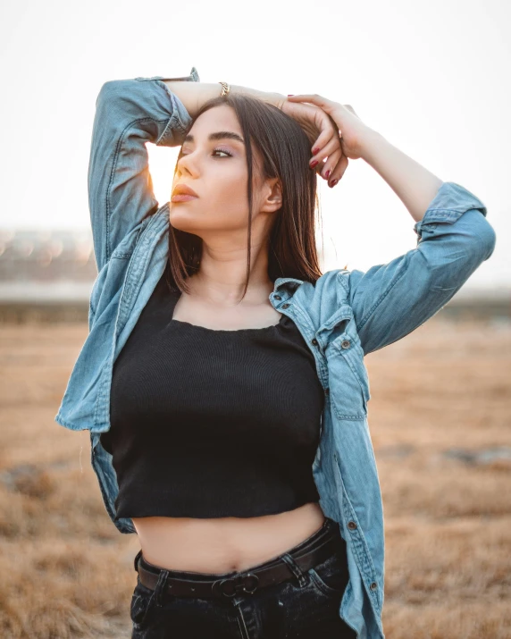 a woman standing in an open field with her hands on her head