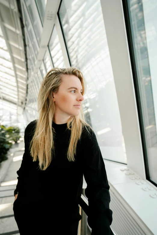 a woman is standing near a window in a large building